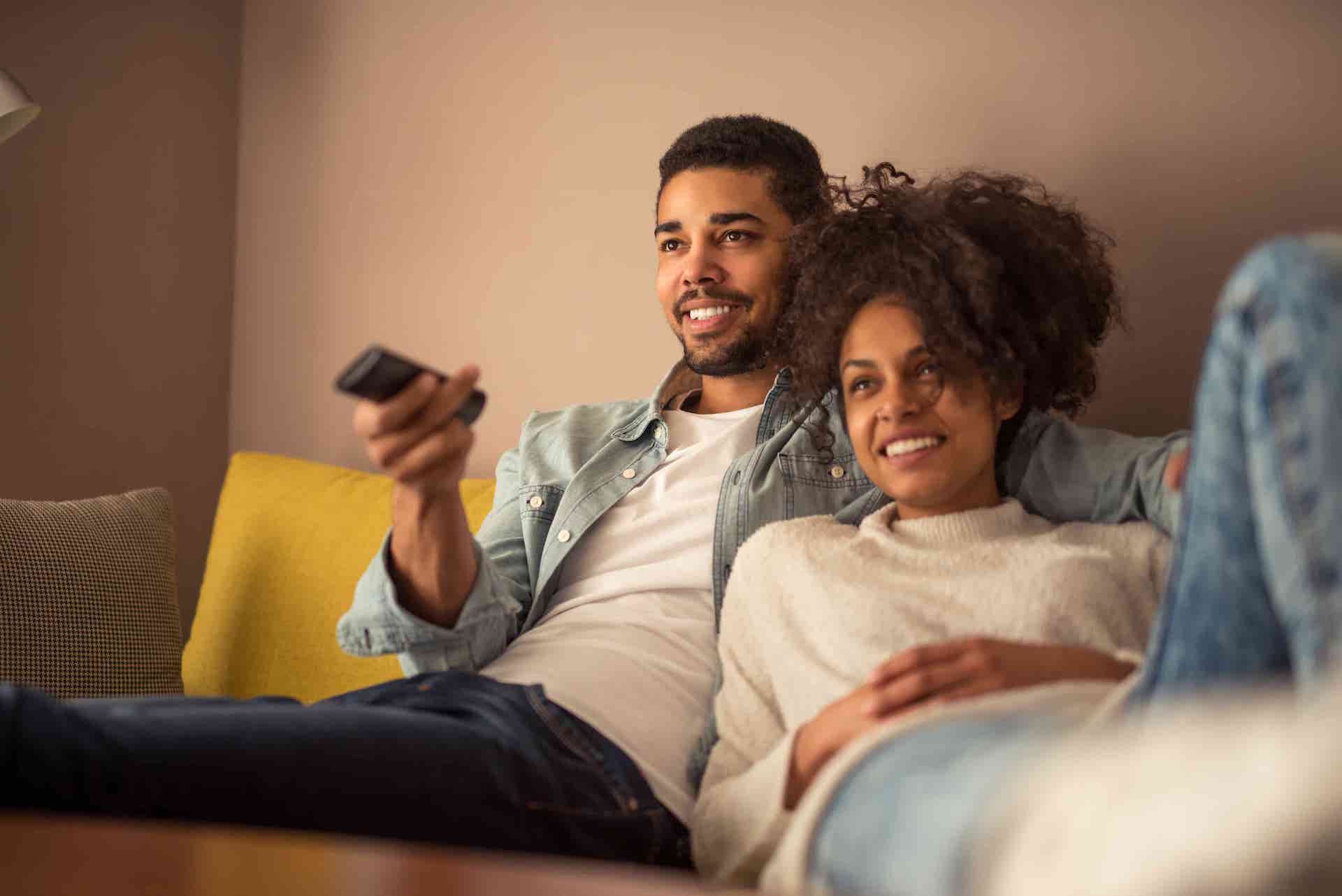 Man and woman lounging on a couch watching television